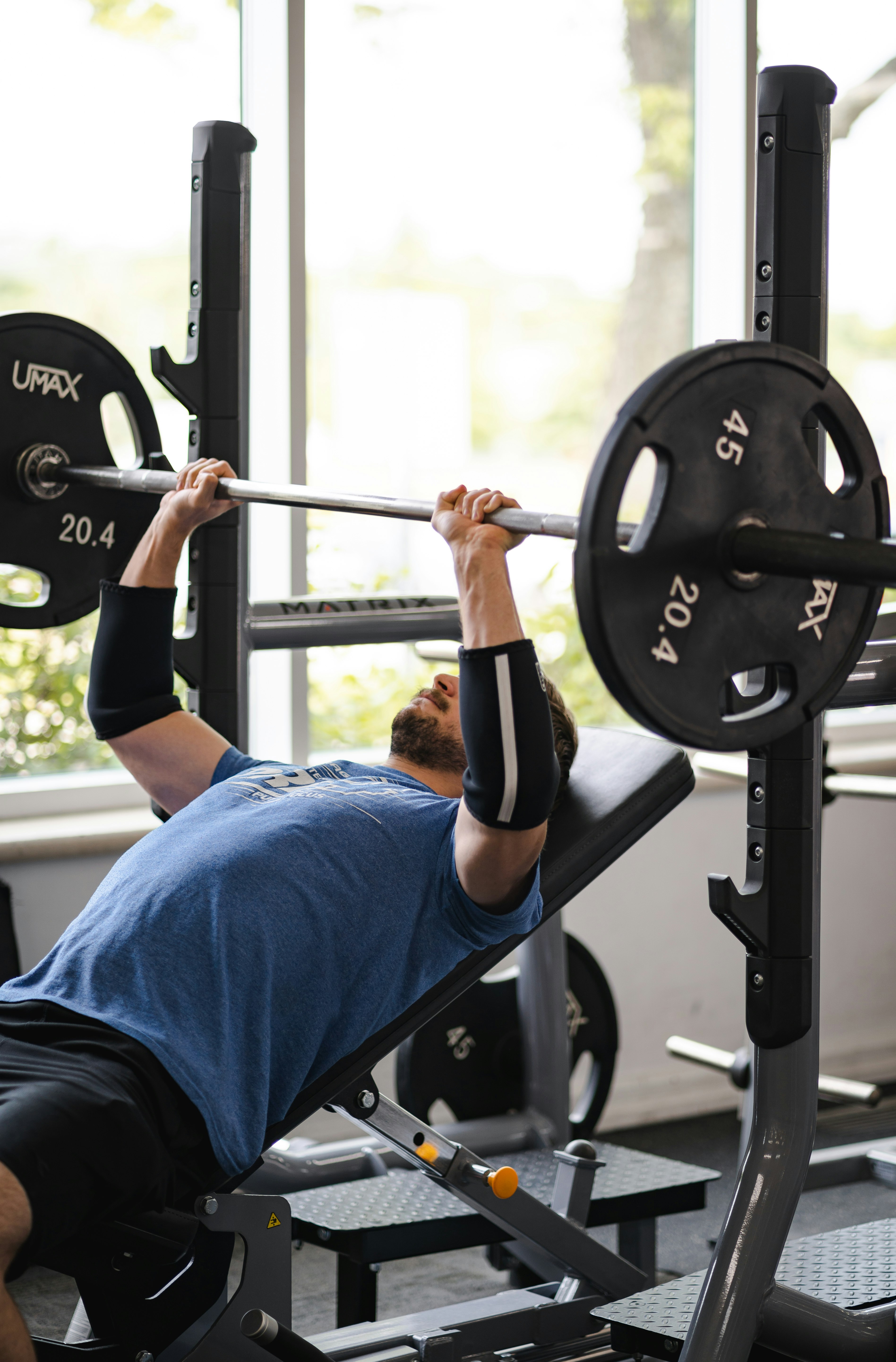 man in blue t-shirt and black pants holding black barbell